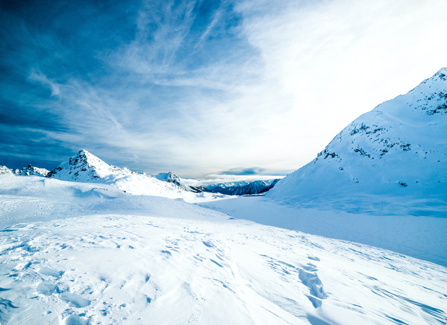 Foot level view of a plateau at the top of a snowy mountain. All surfaces are covered in snow.