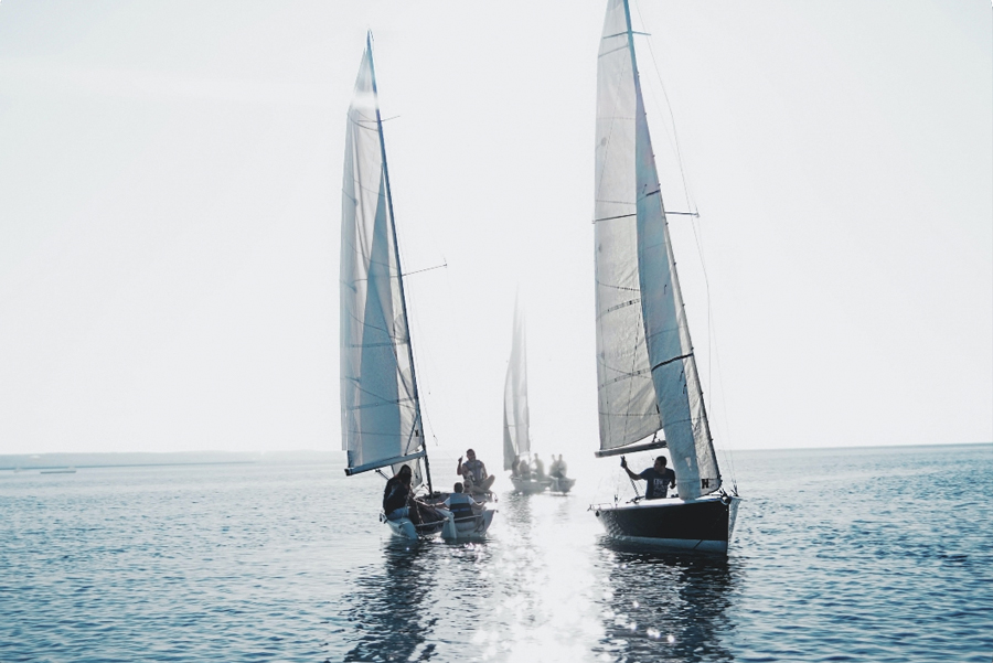 Two sail boats on the open ocean in the forefront with one more small vessel in the background.